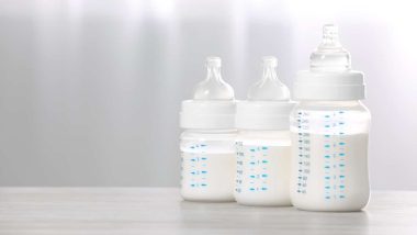 Feeding bottles with infant formula on white wooden table indoors.