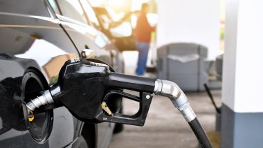 A gasoline pump handle in a gas tank of vehicle with another customer at gas pump in background